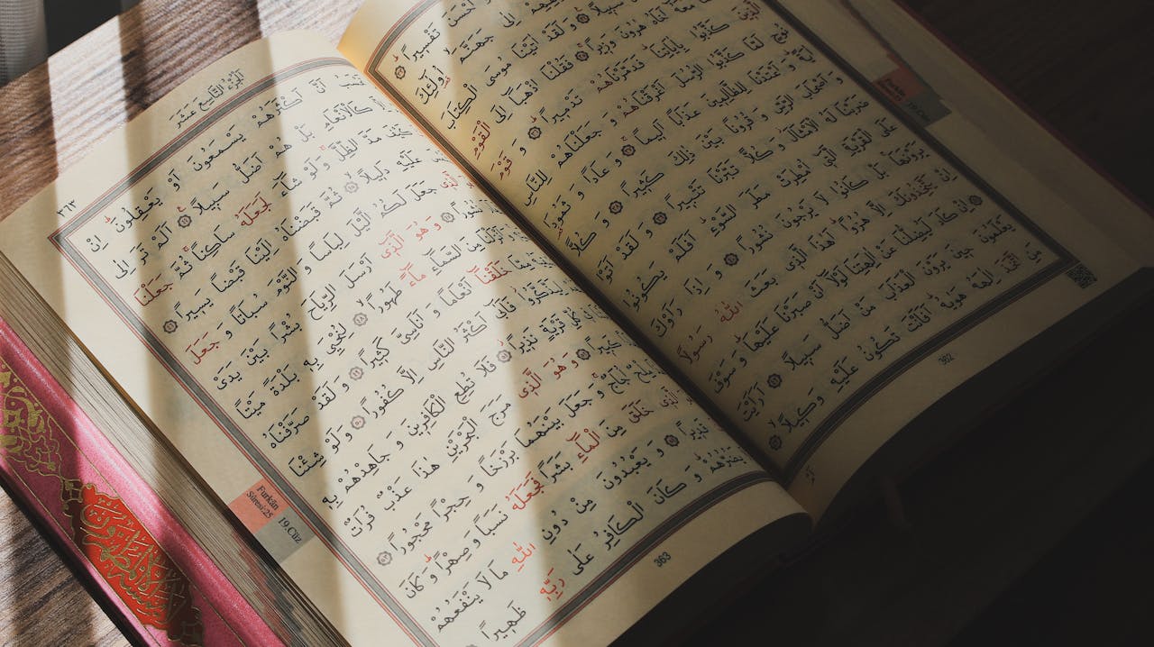 services-03 An open Quran with Arabic script illuminated by natural sunlight on a wooden surface.