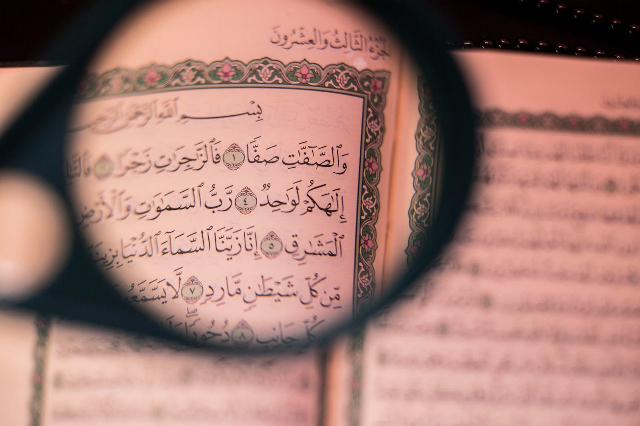 about-01 A detailed view of Arabic text in the Quran, highlighted by a magnifying glass, focusing on Islamic teachings.