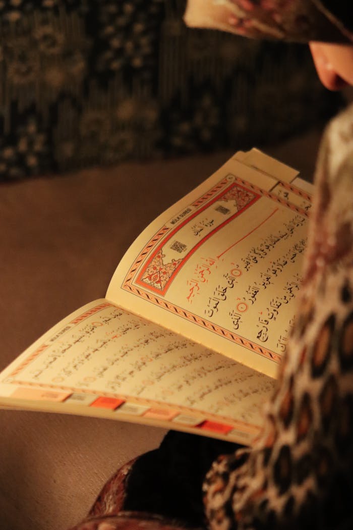 A person reading the Quran in a warm, softly lit indoor setting. Close-up view.