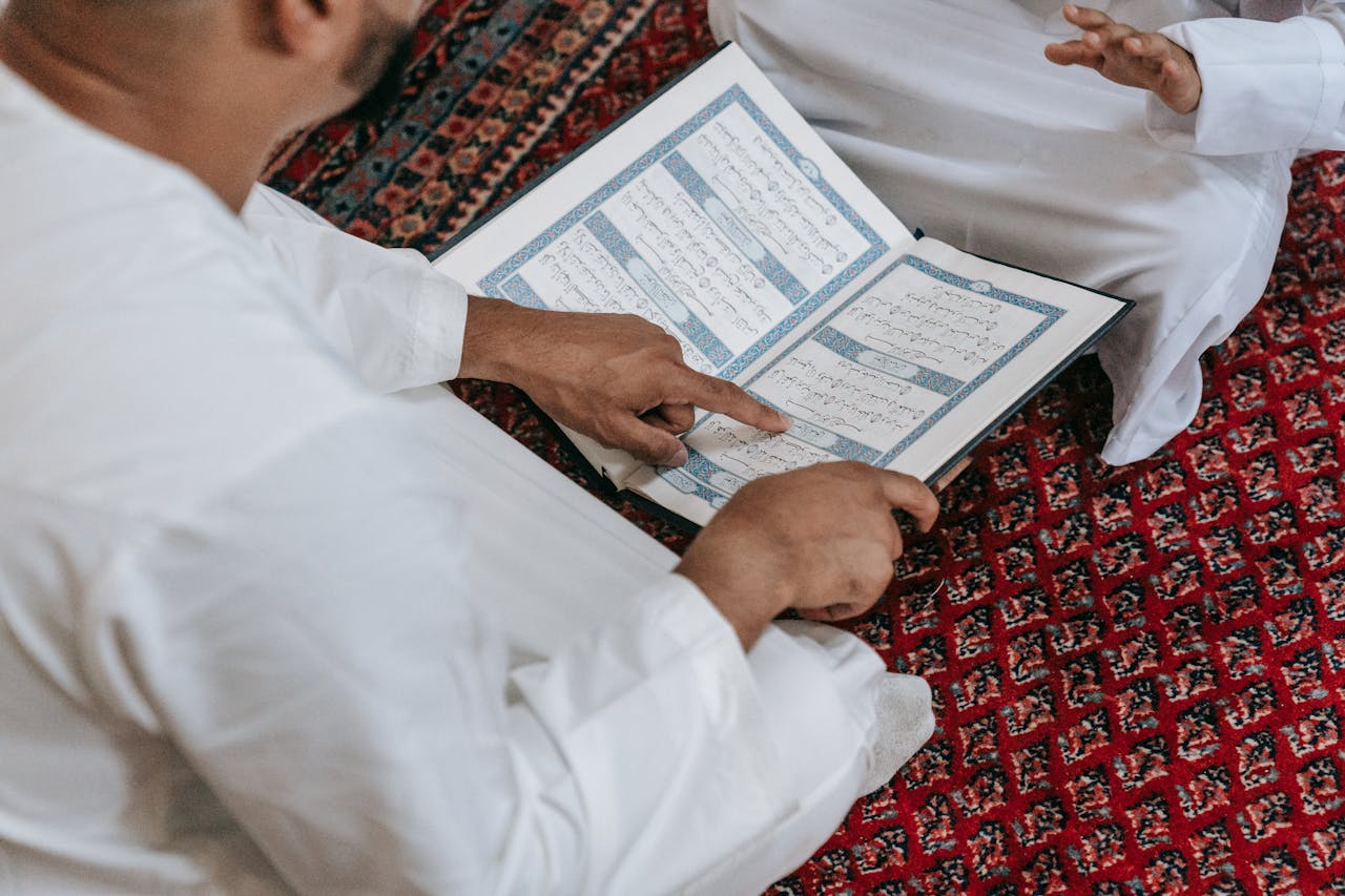 why-choose-us Close-up of two people studying the Quran on a patterned carpet. Religious education setting.